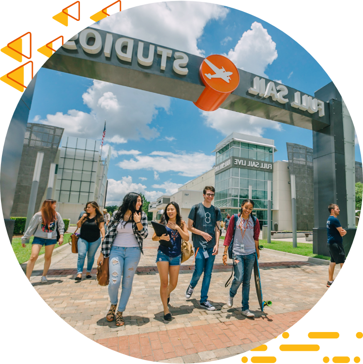 Four students casually chatting and walking under the Full Sail Studios archway, a blue sky with clouds in the background.